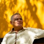 A cheerful man seated against a vibrant yellow wall in Merida, Mexico, enjoying the sunny day.