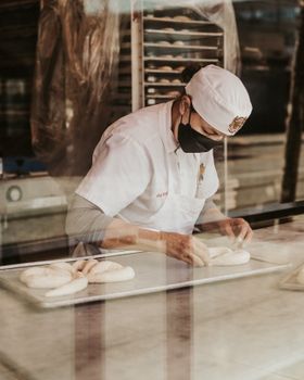 pexels-photo-11869479-11869479 A baker in a white coat and face mask prepares dough in a bakery kitchen.